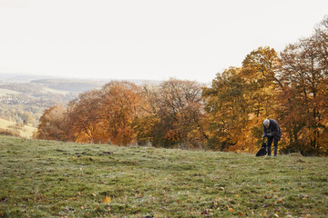 Senior Man Taking Dog For Walk In Autumn Landscape