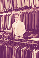 Man seller displaying diverse suits in men’s cloths store