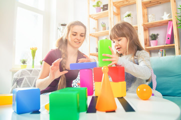 Cute little girl and her mother playing with blocks together, family at home