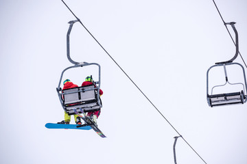 Snowboarder and skier on ski lift seen from below