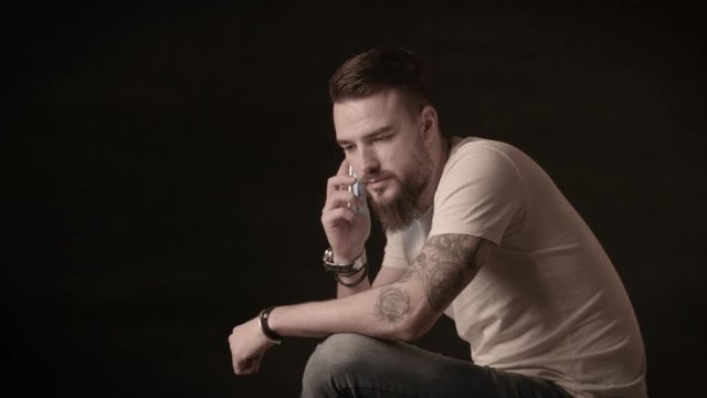 Handsome man with a beard talking on the phone in a studio on a black background
