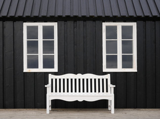Fototapeta na wymiar weiße Parkbank vor schwarzem Holzhaus in hofsos in Island