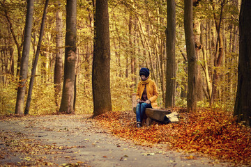 Fototapeta premium Young stylish hipster girl sitting on the bench in the autumn park and reading electronic book