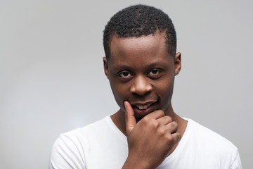 Portrait of young afroamerican man looking at the camera. Cunning, plotting, sly, crafty guy on grey background with free space for text.