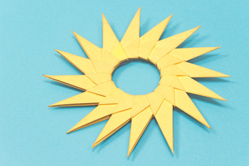 Origami yellow paper sun isolated on blue background