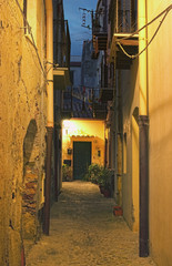 A narrow street stretches to the front doors of a pretty house. Cefalu. Sicily. Italy
