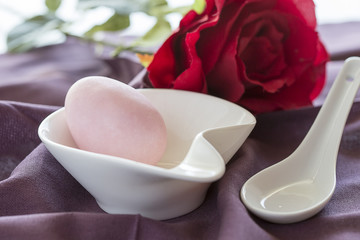 Uovo di zucchero rosa dentro a contenitore bianco e sullo sfondo una rosa rossa