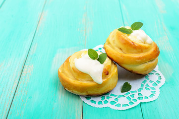 Freshly baked, cottage cheese buns, with cream and mint leaves on a white napkin on a light background.