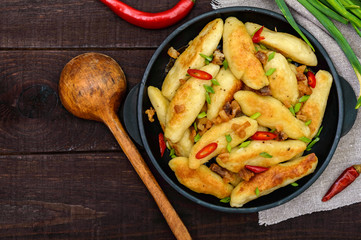 Popular traditional Czech, Hungarian, German dish: potato knedli (dumplings) with slices of fried bacon, spicy red pepper and green onions. Serving on a cast iron pan. The top view