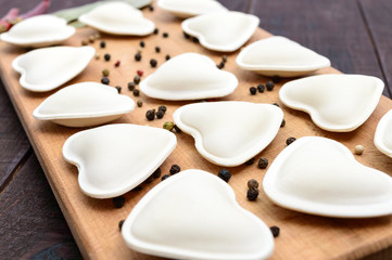 Uncooked dough in the shape of a heart (dumplings, ravioli, pelmeni), on a cutting board. Close up