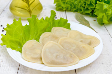 Italian ravioli (dumplings) in the shape of a heart on a plate on white wooden background.