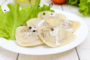 Italian ravioli (dumplings) in the shape of a heart on a plate on white wooden background.
