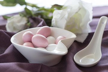 Ovetti di zucchero rosa e bianchi dentro a contenitore bianco e sullo sfondo una rosa bianca