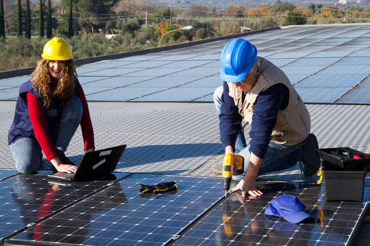 Young Engineer Girl And An Elderly Skilled Worker Fitting A Photovoltaic Plant