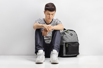 Sad teenage student leaning against a gray wall
