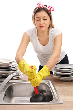 Young Woman Using A Plunger To Unclog A Sink