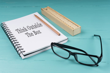 Notebook, pencil, wooden ruler and glasses on the blue wooden background with words Think Outside The Box. Top View. Business Concept.