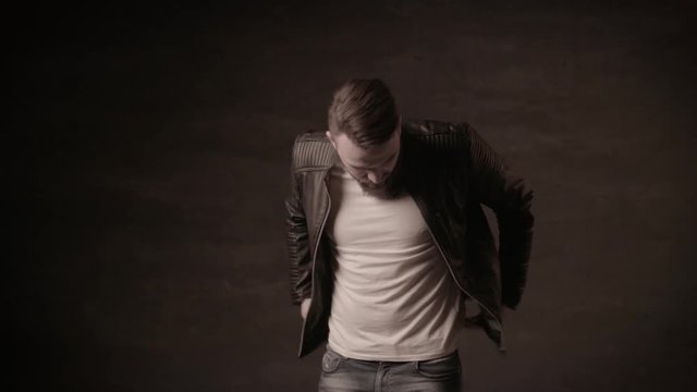Handsome man with a beard in a black leather jacket posing in the studio on a black background