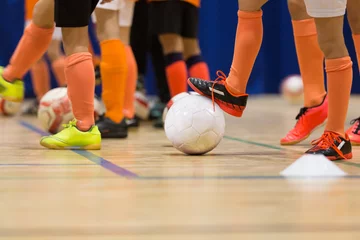 Foto op Plexiglas Voetbal Zaalvoetbaltraining voor kinderen. Indoor voetbal jonge speler met een voetbal in een sporthal. Sport achtergrond.