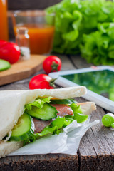 Sandwich with red fish and cucumbers on a table with a tablet, selective focus