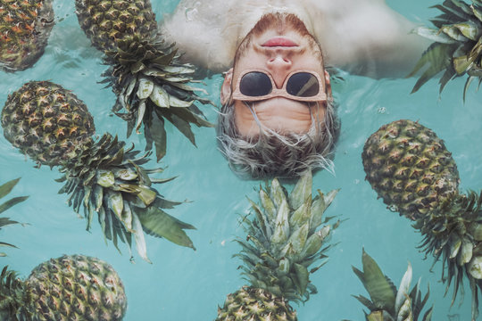 Young man in swimming pool surrounded by pineapples