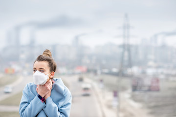 Young woman in protective mask feeling bad in the city with air pollution from traffic and...