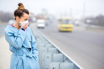 Young woman in protective mask feeling bad on the street in the city with air pollution