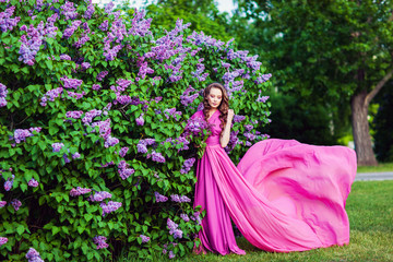 Obraz na płótnie Canvas Young beautiful girl posing near lilac bushes in blossom