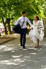 Happy wedding couple runs along the path under green trees