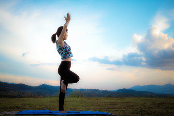 Fototapeta na wymiar Woman practicing yoga pose outdoors over sunset sky background.