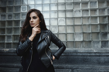 Eastern beautiful woman wearing biker jacket poses in backyard of vintage apartment house