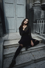 Eastern beautiful woman wearing biker jacket poses in backyard of vintage apartment house