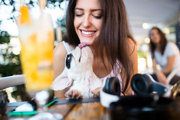 Beautiful young woman sitting in cafe with her adorable French bulldog puppy. Spring or summer city...