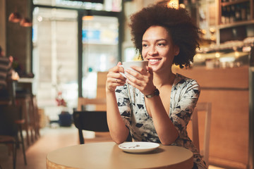 Mixed race woman in coffee shop having cofe and smiling