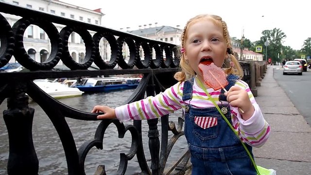 Charm little girl walking along the river embankment sucking lollipop