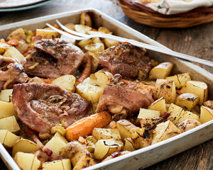 Baked turkey sliced leg in a baking tray with potatoes, onion and carrots on an old wooden table