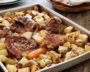 Baked turkey sliced leg in a baking tray with potatoes, onion and carrots on an old wooden table