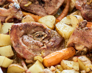 Baked turkey sliced leg in a baking tray with potatoes, onion and carrots on an old wooden table
