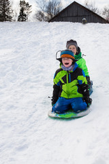 Fototapeta na wymiar Boys riding a sled, tobogganing down the snow