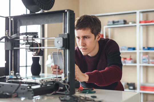 A man graphic designer taking photo of 3d printing process with cell phone.