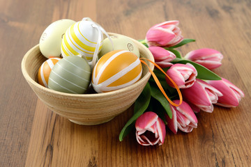 Easter eggs in cup with bunch of pink tulips wooden background