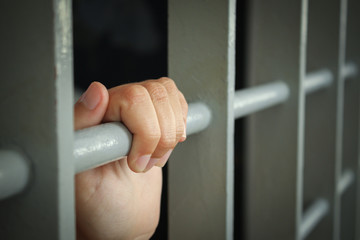 Woman's hands holding the bars of a cell