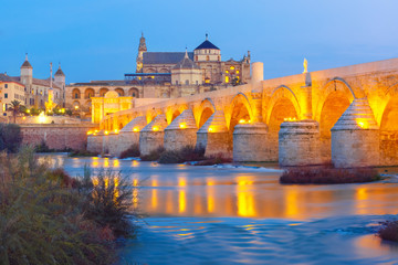Obraz premium Illuminated Great Mosque Mezquita - Catedral de Cordoba with mirror reflection and Roman bridge across Guadalquivir river during evening blue hour, Cordoba, Andalusia, Spain