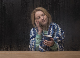 Young woman talking on the phone looking through a window on a rainy day
