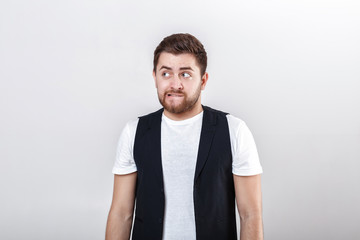 portrait of handsome pensive brunette man in white shirt on gray background. guy thinks