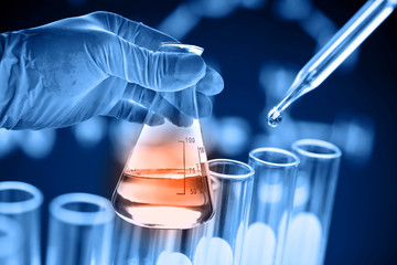 Flask in scientist hand with test tubes in laboratory  