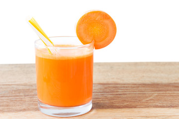 Fresh carrot juice in glass with straw on wooden table, white background.