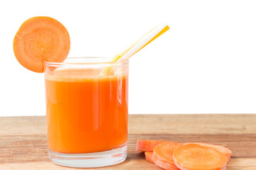 Fresh carrot juice in glass with straw and slices carrot vegetable on wooden table, white background