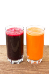 Two glass of fresh beet and carrot juice on wooden table, white background.
