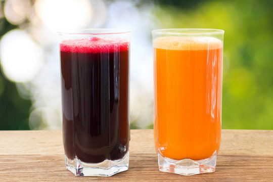 Two glass of fresh beet and carrot juice on wooden table, defocused, nature background.